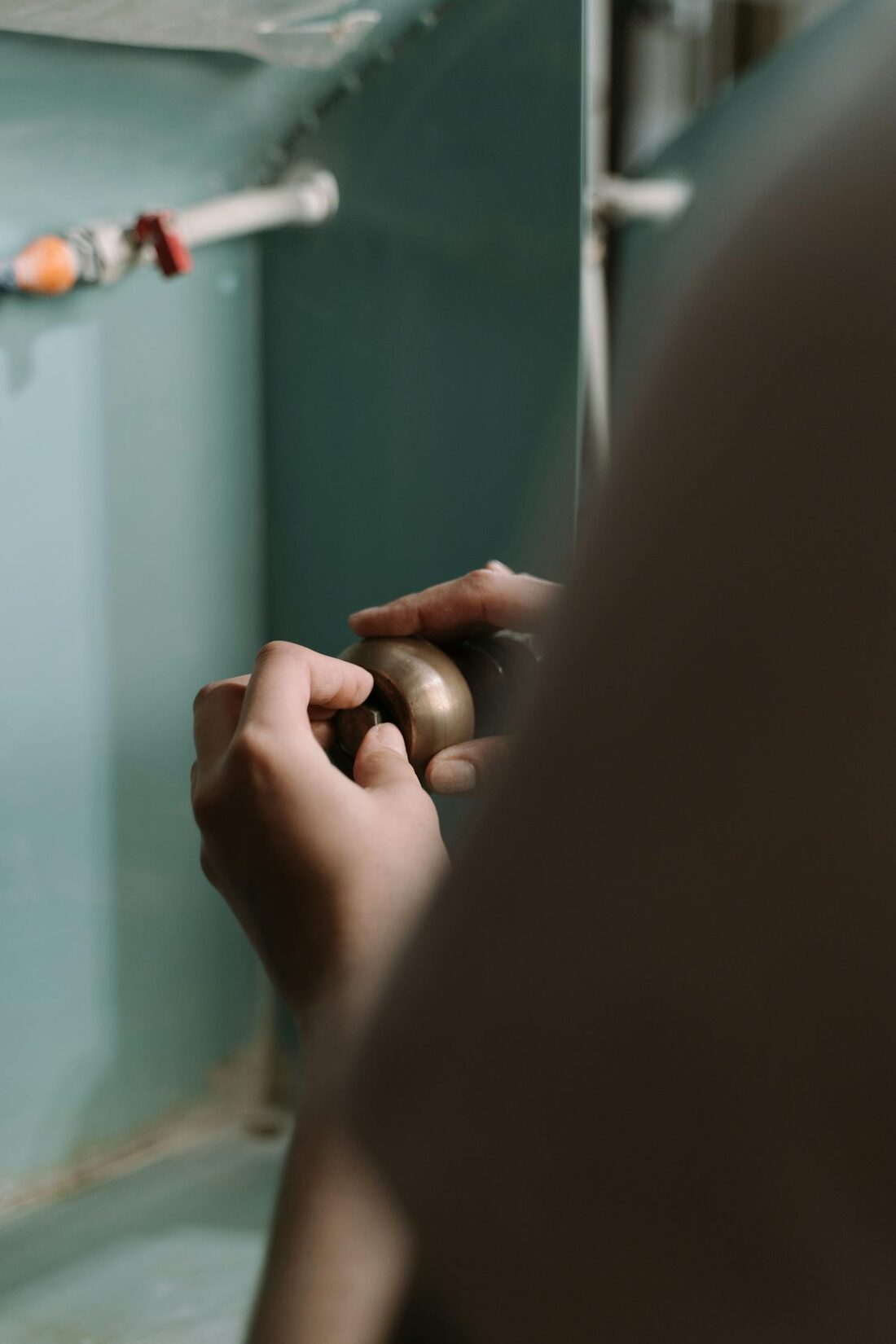 A plumber's hands fitting a brass valve onto residential pipework